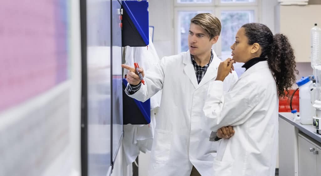 Two researchers in lab coats collaborating in front of whiteboard