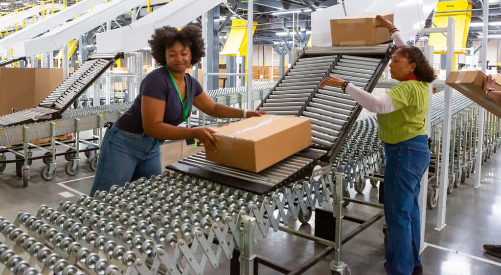 Two workers in a factory assisting boxed product down rollers