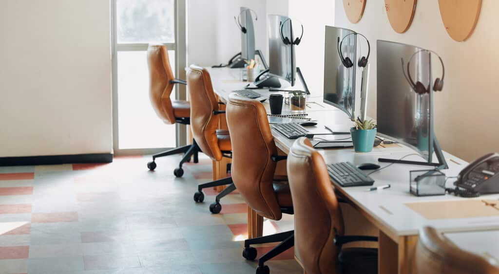 Photo of four workstations with chairs, keyboards, monitors, and headsets that appear to be in a call center environment