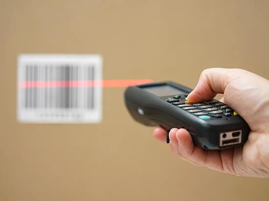 closeup of hand holding bar code scanner and scanning code on cardboard box