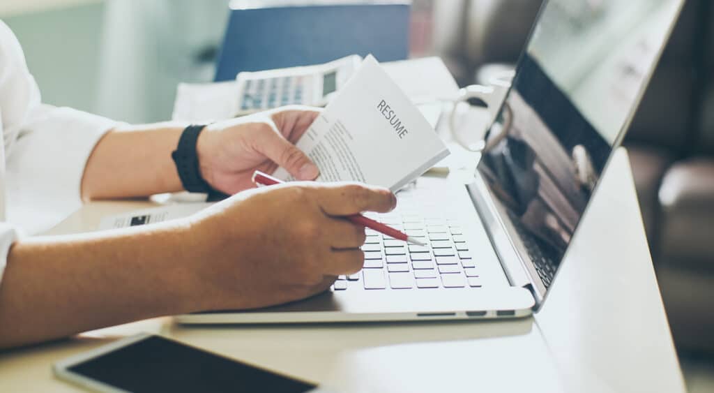 Photo agrandie de mains tenant un CV et un stylo à encre rouge