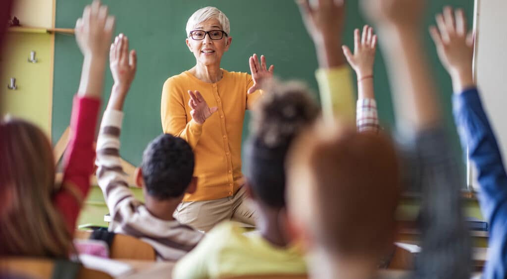 Photo d'un enseignant face à une salle pleine d'étudiants avec les mains levées