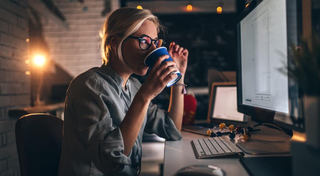 Mujer mirando la pantalla de la computadora con un lienzo en blanco bebiendo de una taza