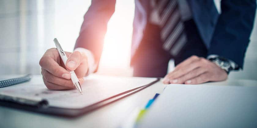 Person in a suit writing in a notebook with a pen