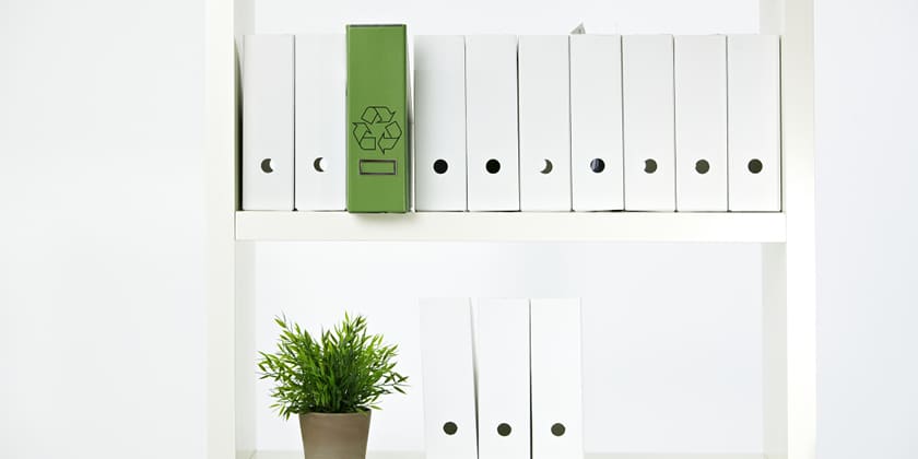 White binders on a shelf with one green recycling binder