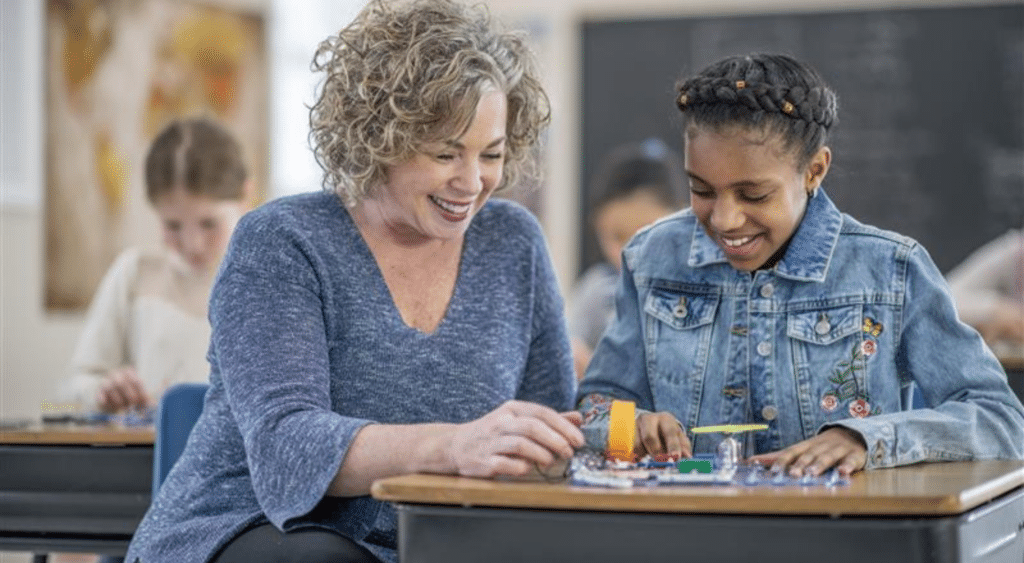 educator with student working on project at desk smiling